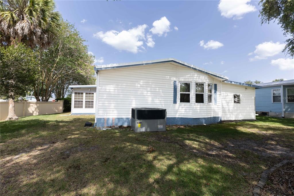 The exterior of a white mobile home features a central air conditioning unit and lawn — 1159 PARADISE DRIVE, LADY LAKE, FL