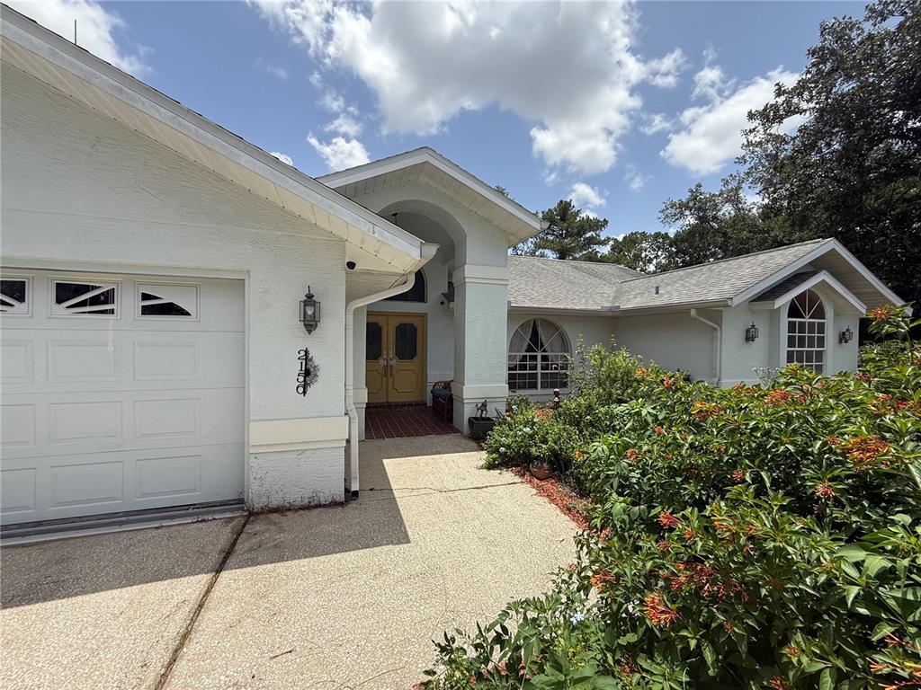 A white stucco house with a garage, arched entryway, and a front garden — 2156 NEW AZORA ROAD, SPRING HILL, FL