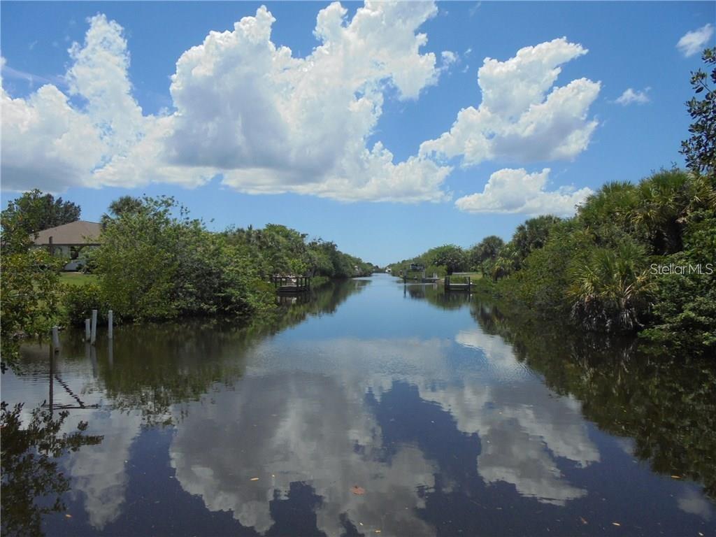 A narrow canal flows between lush green vegetation and wooden docks under a cloudy sky — 5087 SILVER BELL DRIVE, PORT CHARLOTTE, FL