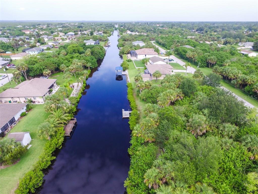 An aerial view shows a canal flowing between residential properties surrounded by dense green vegetation — 5087 SILVER BELL DRIVE, PORT CHARLOTTE, FL