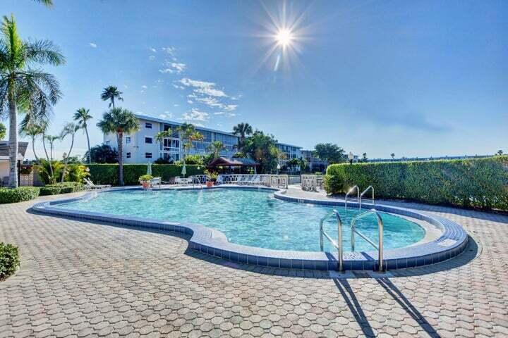 A kidney-shaped swimming pool sits on a paved patio in front of a multi-story building — 2566 GARDEN Drive S # 306, Lake Worth FL 33461, LAKE WORTH, FL
