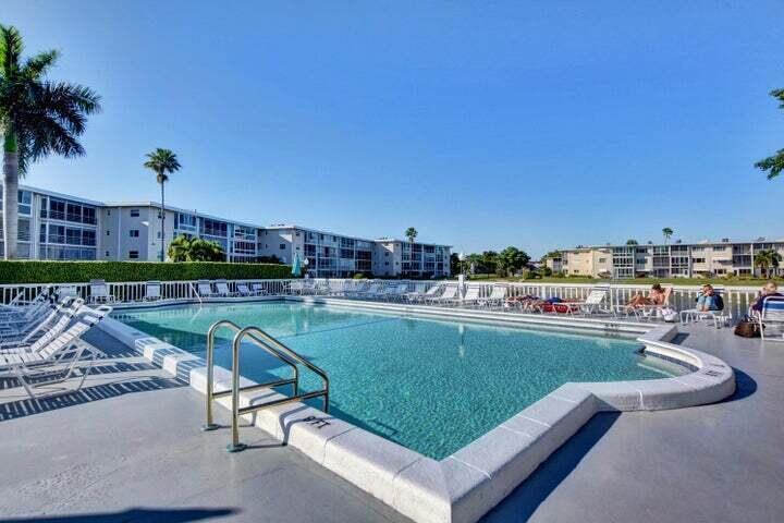 A rectangular swimming pool sits on a concrete deck surrounded by lounge chairs and buildings — 2566 GARDEN Drive S # 306, Lake Worth FL 33461, LAKE WORTH, FL