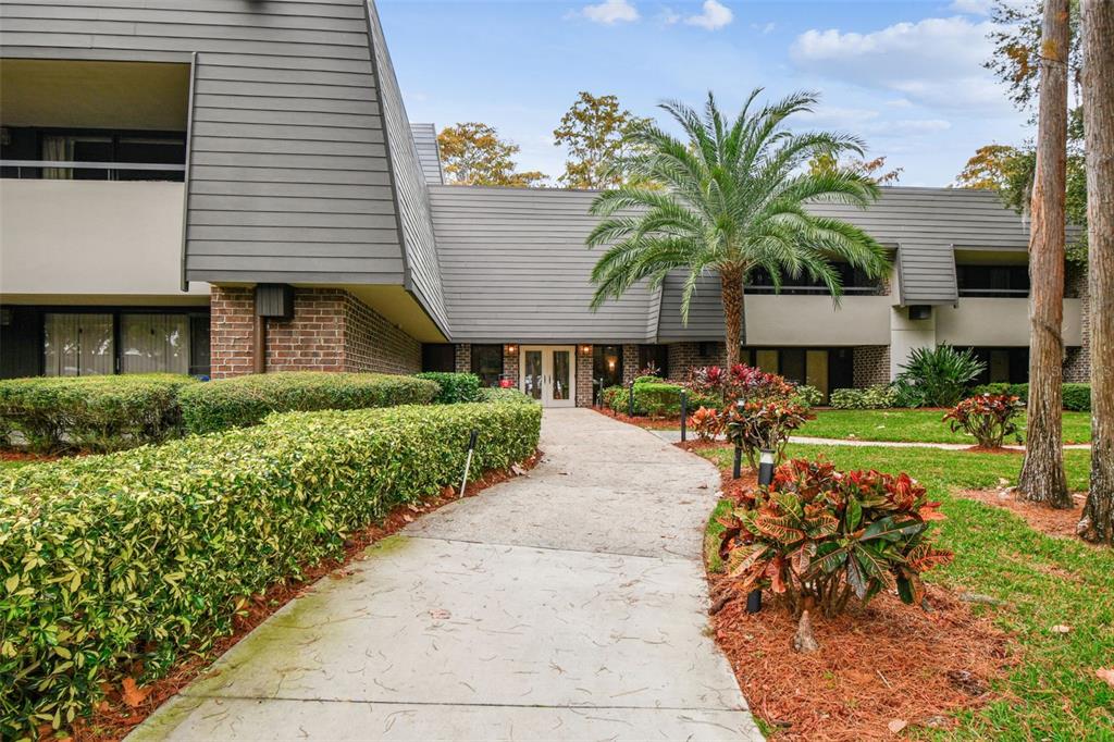 A concrete walkway leads to the entrance of a two-story building with gray siding — 36750 US HIGHWAY 19 N UNIT 03106, PALM HARBOR, FL