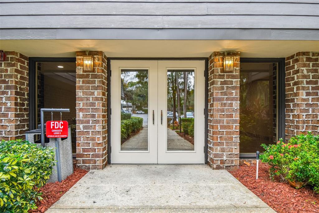 A brick building entrance features double glass doors, two wall-mounted lights, and a fire department connection — 36750 US HIGHWAY 19 N UNIT 03106, PALM HARBOR, FL