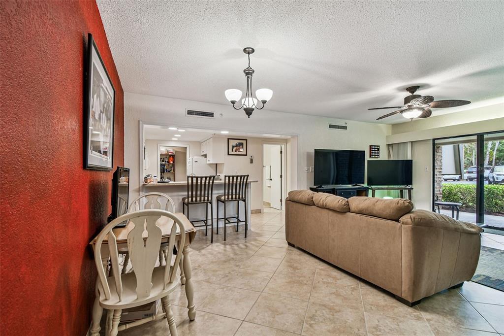 A living room with a beige sofa, tiled floors, a red accent wall, and kitchen access — 36750 US HIGHWAY 19 N UNIT 03106, PALM HARBOR, FL
