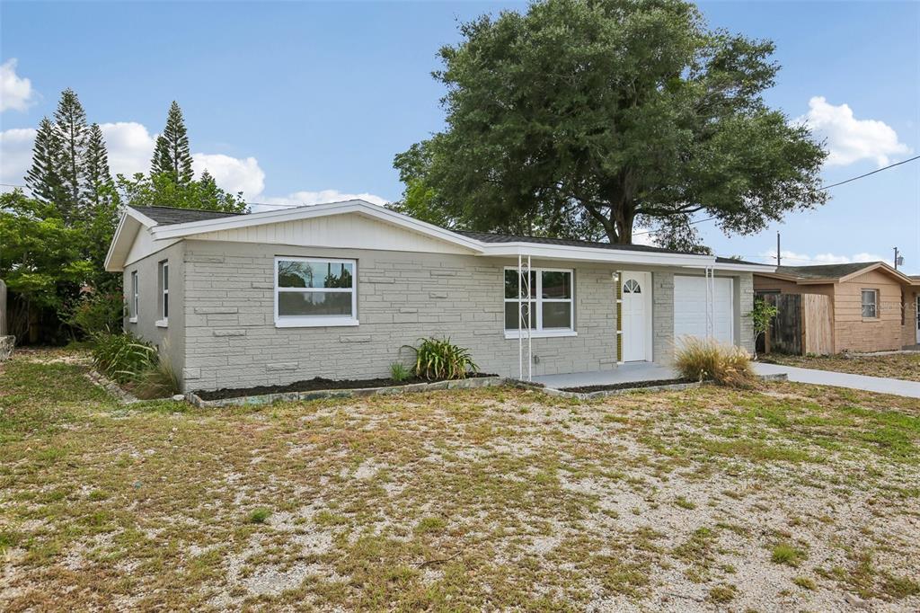 A single-story house with gray brick siding, a white front door, and a gravel yard — 4922 PANORAMA AVENUE, HOLIDAY, FL