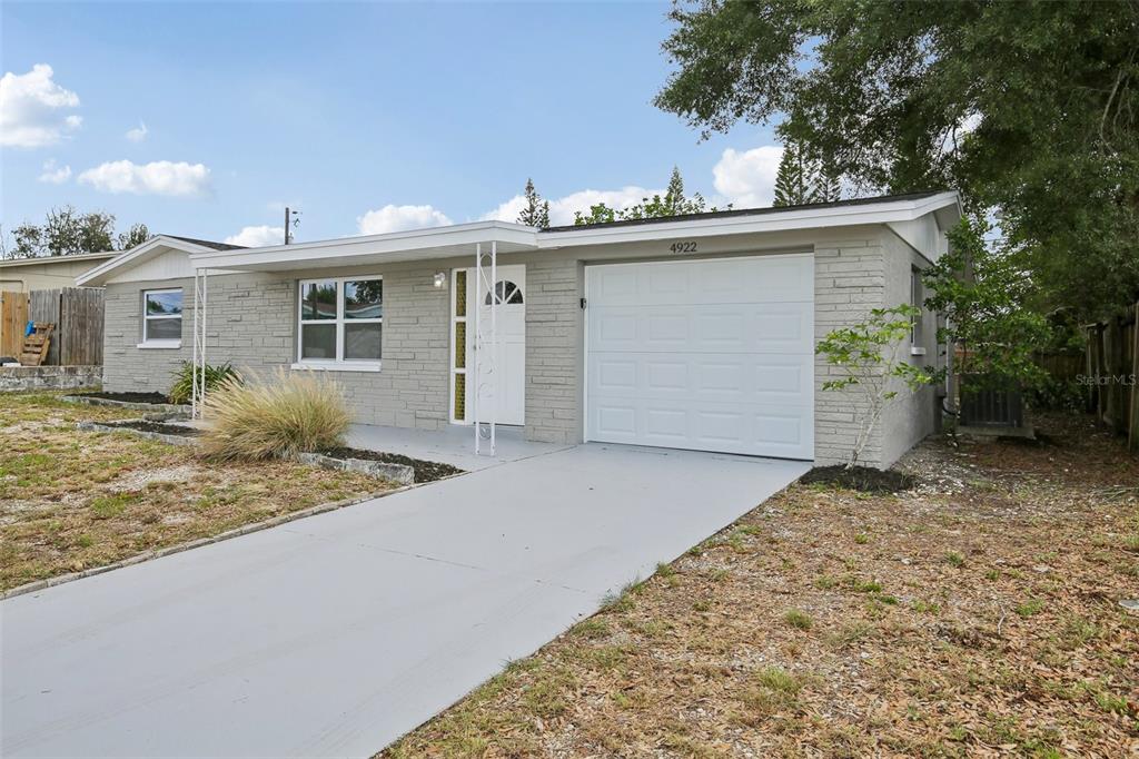 A single-story house with a gray brick exterior, white garage door, and a concrete driveway — 4922 PANORAMA AVENUE, HOLIDAY, FL