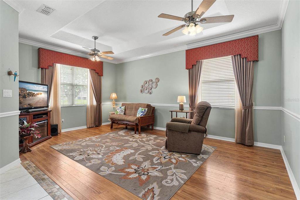 A living room with light green walls, wood flooring, two ceiling fans, and patterned window valances — 36403 GRAND ISLAND OAKS CIRCLE, GRAND ISLAND, FL