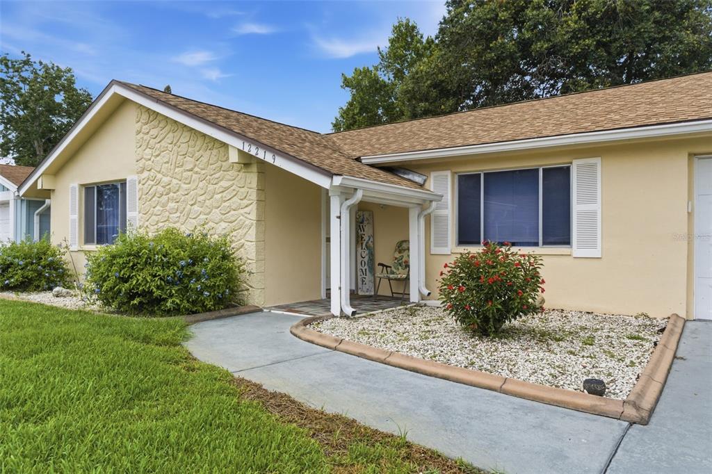 A single-story house with a beige exterior, stone accent wall, and a covered front entryway — 12219 QUAIL RUN ROW, BAYONET POINT, FL