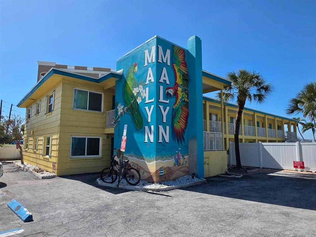 A two-story yellow motel building features a large mural of parrots on its corner exterior — 282 TREASURE ISLAND CAUSEWAY UNIT 12, TREASURE ISLAND, FL