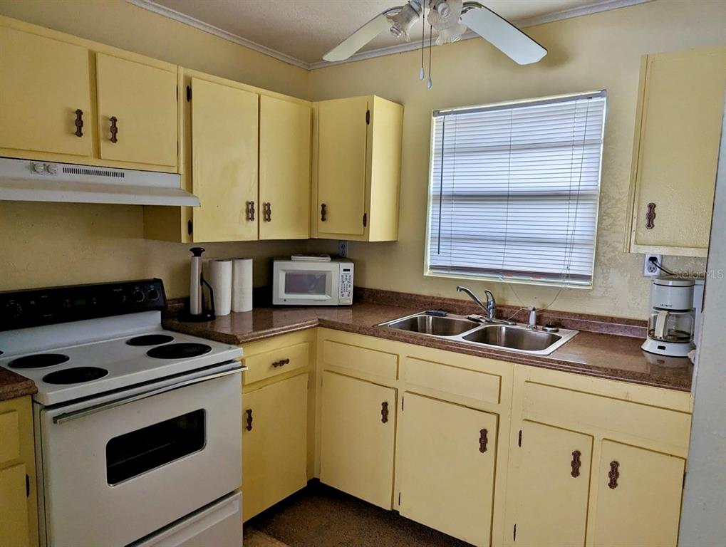 A kitchen features yellow cabinets, a white stove, a double sink, and a ceiling fan — 25130 NE 132ND LANE, SALT SPRINGS, FL