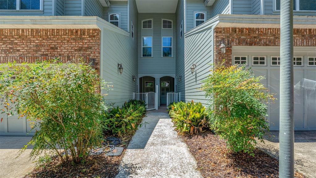 A concrete walkway leads to the shared entrance of a two-story townhouse with brick accents — 1852 NW 34TH STREET UNIT 24, GAINESVILLE, FL