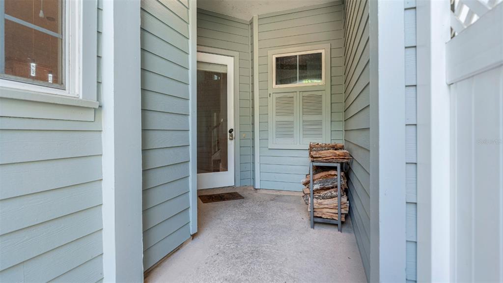 A covered outdoor patio features light blue siding, a glass door, and a firewood rack — 1852 NW 34TH STREET UNIT 24, GAINESVILLE, FL