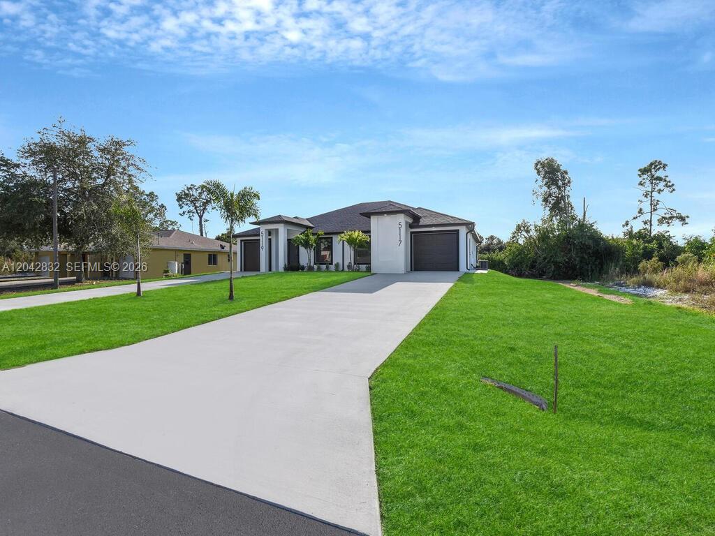 A modern single-story house with a concrete driveway and a green lawn — 5117 24th St SW, Lehigh Acres FL 33973, LEHIGH ACRES, FL