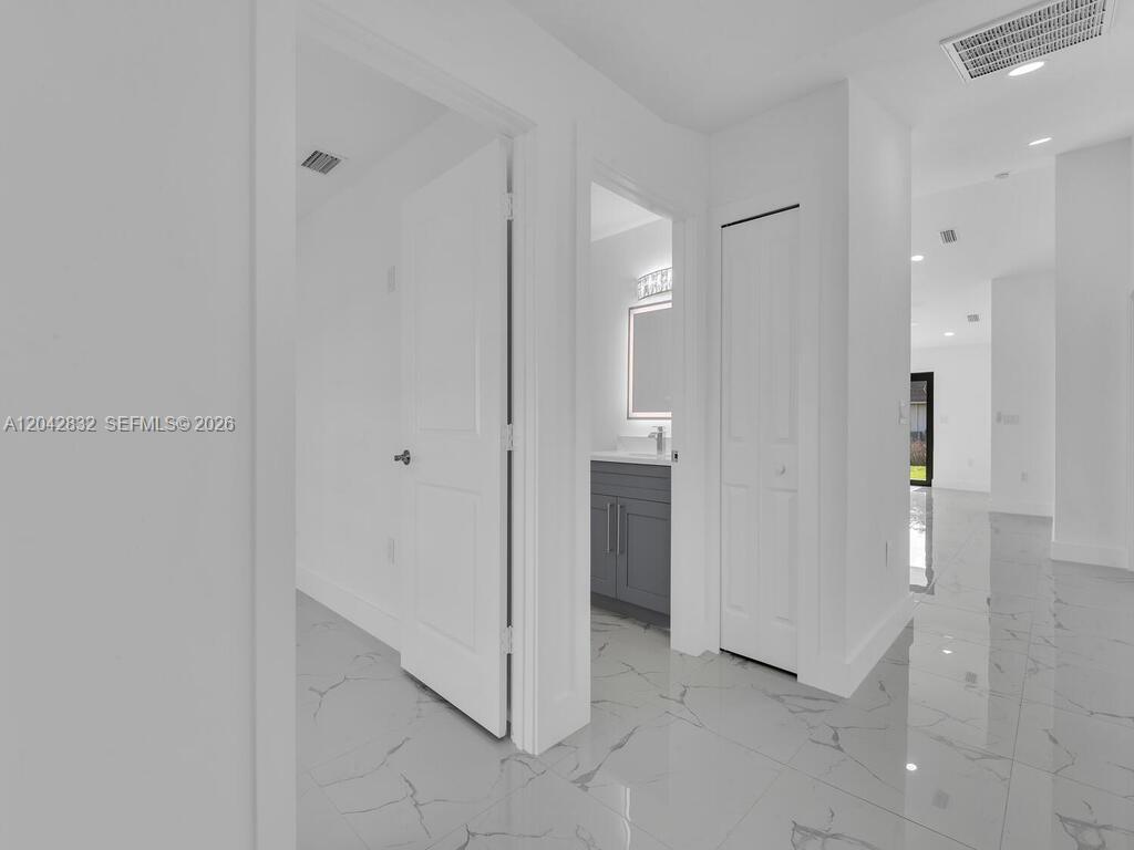 A hallway with white walls and marble-patterned tile flooring leads to a bathroom and living area — 5117 24th St SW, Lehigh Acres FL 33973, LEHIGH ACRES, FL