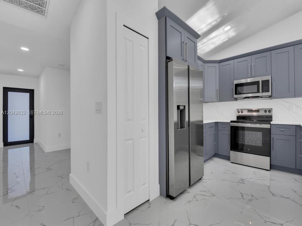 A modern kitchen features gray cabinets, stainless steel appliances, and white marble-patterned tile flooring — 5117 24th St SW, Lehigh Acres FL 33973, LEHIGH ACRES, FL