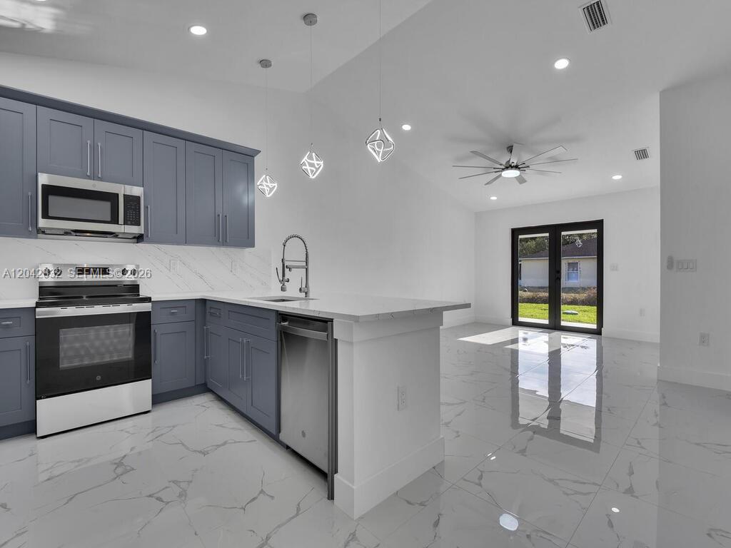 A modern kitchen features blue cabinets, white countertops, and marble-patterned tile flooring — 5117 24th St SW, Lehigh Acres FL 33973, LEHIGH ACRES, FL