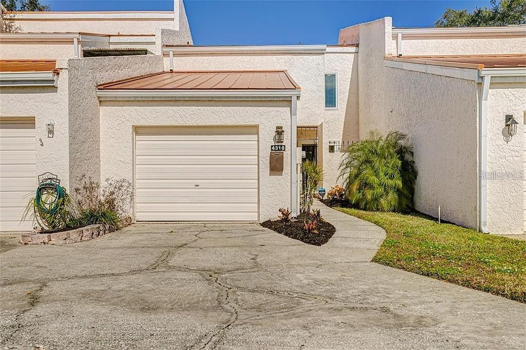 A beige townhouse exterior features a single-car garage, a concrete driveway, and a front entrance — 4316 SUNRAY COURT UNIT 34, TAMPA, FL