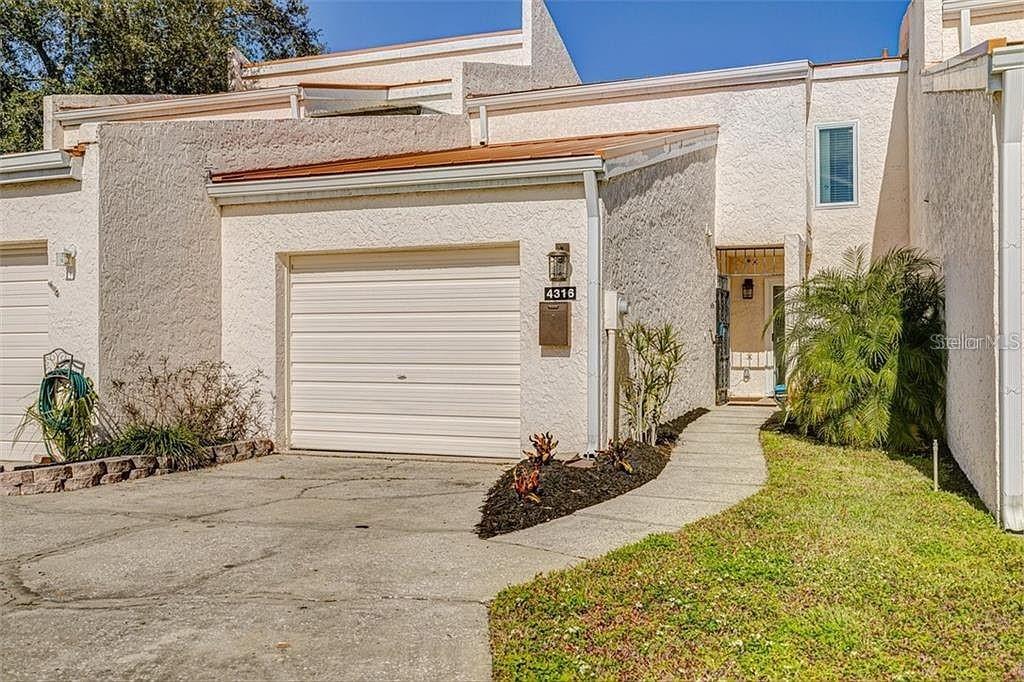A stucco townhome exterior features a single-car garage, a concrete driveway, and a front entryway — 4316 SUNRAY COURT UNIT 34, TAMPA, FL