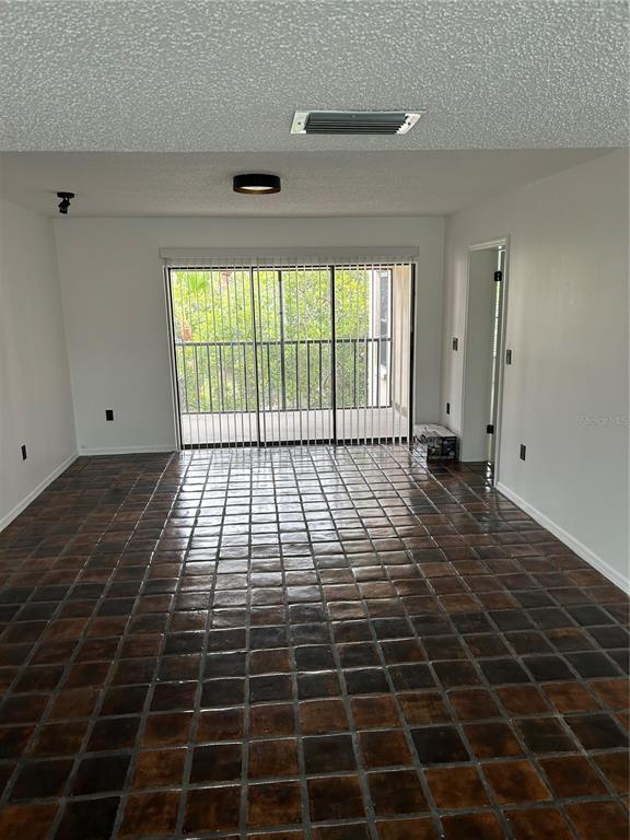 An empty room features dark, square-tiled flooring, white walls, and a sliding glass door — 2462 KINGFISHER LANE UNIT J203, CLEARWATER, FL