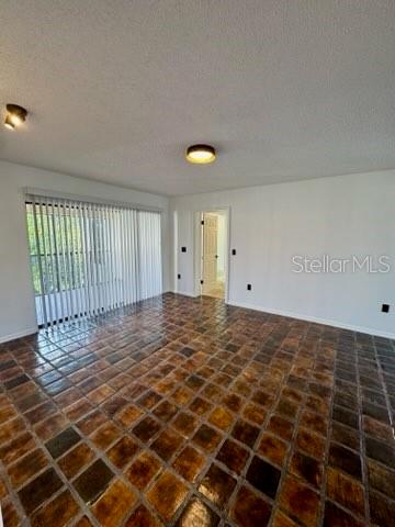 An empty room features dark, multi-toned square floor tiles, white walls, and vertical window blinds — 2462 KINGFISHER LANE UNIT J203, CLEARWATER, FL