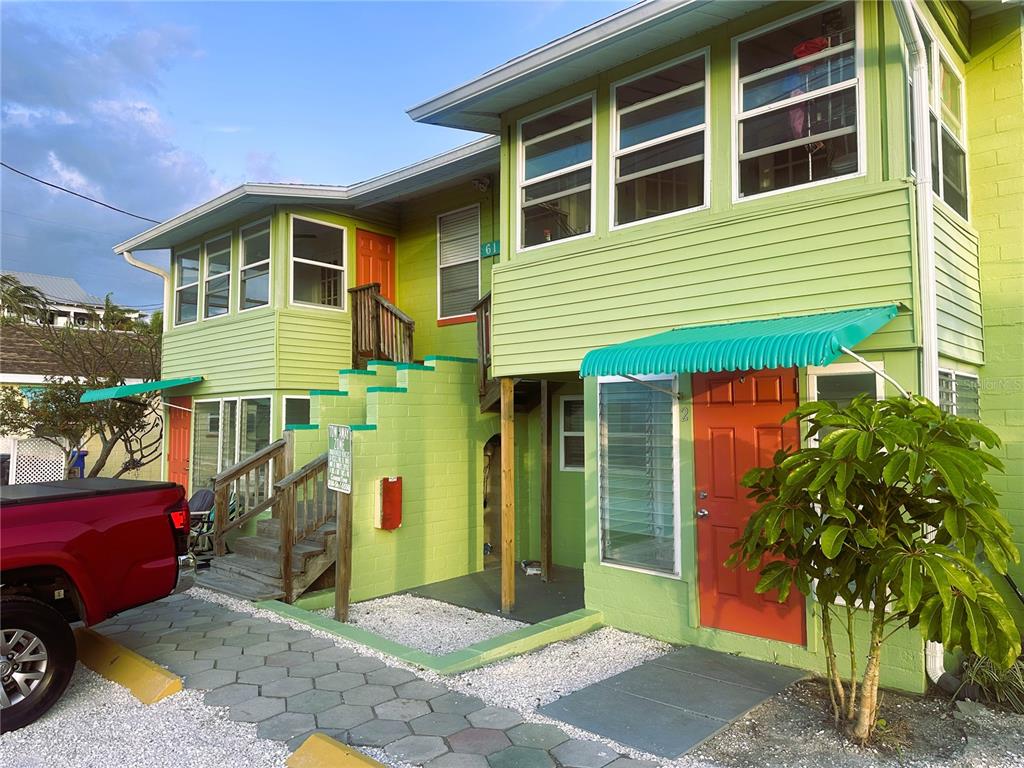 A two-story lime green building with orange doors, exterior stairs, and a paved parking area — 61 81ST AVENUE UNIT 2, TREASURE ISLAND, FL
