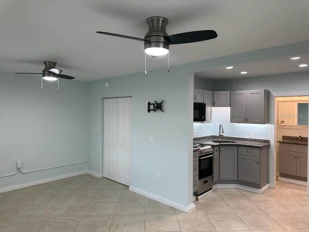 A room with light blue walls, two ceiling fans, and an adjacent gray-cabinet kitchen — 61 81ST AVENUE UNIT 2, TREASURE ISLAND, FL