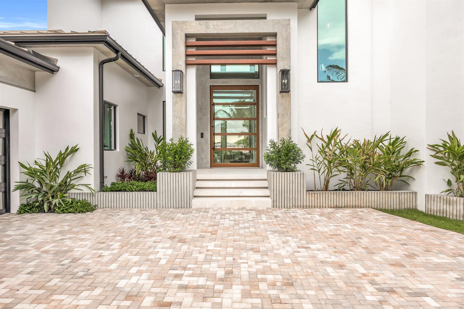 The exterior of a modern home features a paved driveway, concrete planters, and a glass door — 19175 W Riverside Drive, Tequesta FL 33469, TEQUESTA, FL