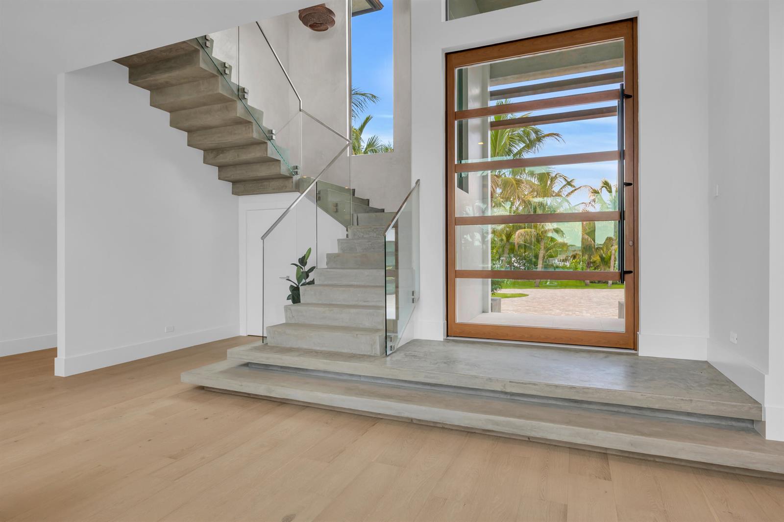 A modern entryway features concrete stairs with glass railings and a large wood-framed glass door — 19175 W Riverside Drive, Tequesta FL 33469, TEQUESTA, FL