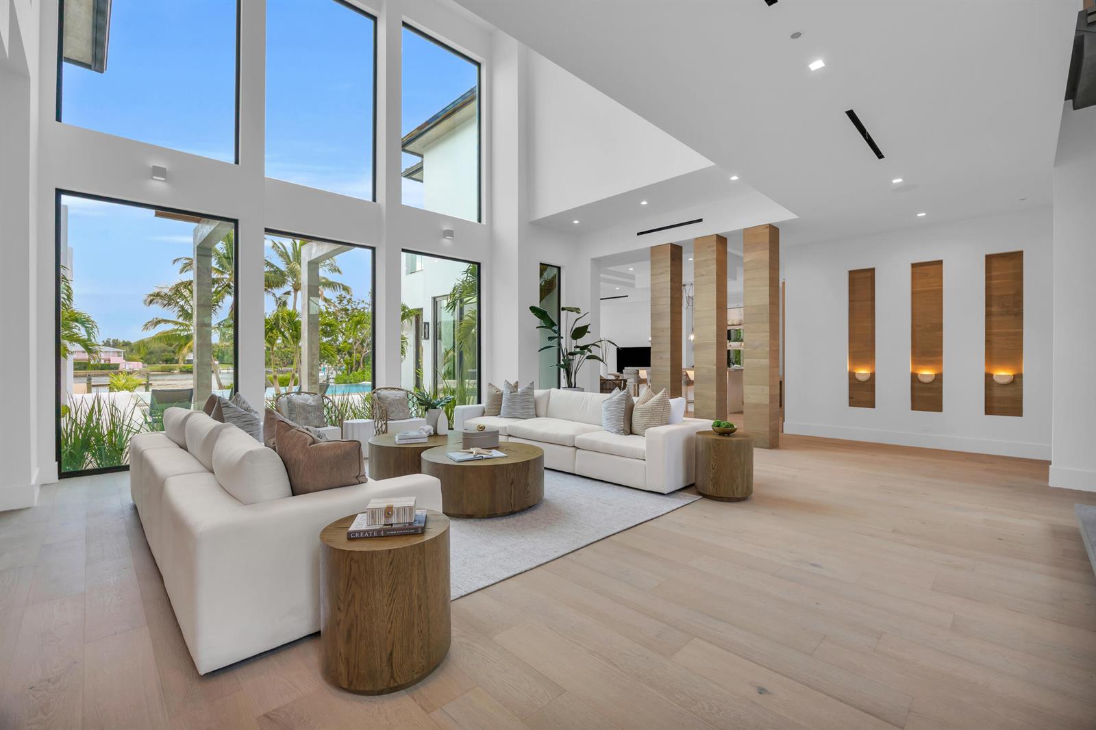 A bright living room features high ceilings, floor-to-ceiling windows, white sofas, and wood accents — 19175 W Riverside Drive, Tequesta FL 33469, TEQUESTA, FL