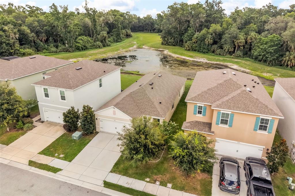 An aerial view shows three suburban houses with driveways facing a pond and wooded area — 289 GINA LANE, DAVENPORT, FL