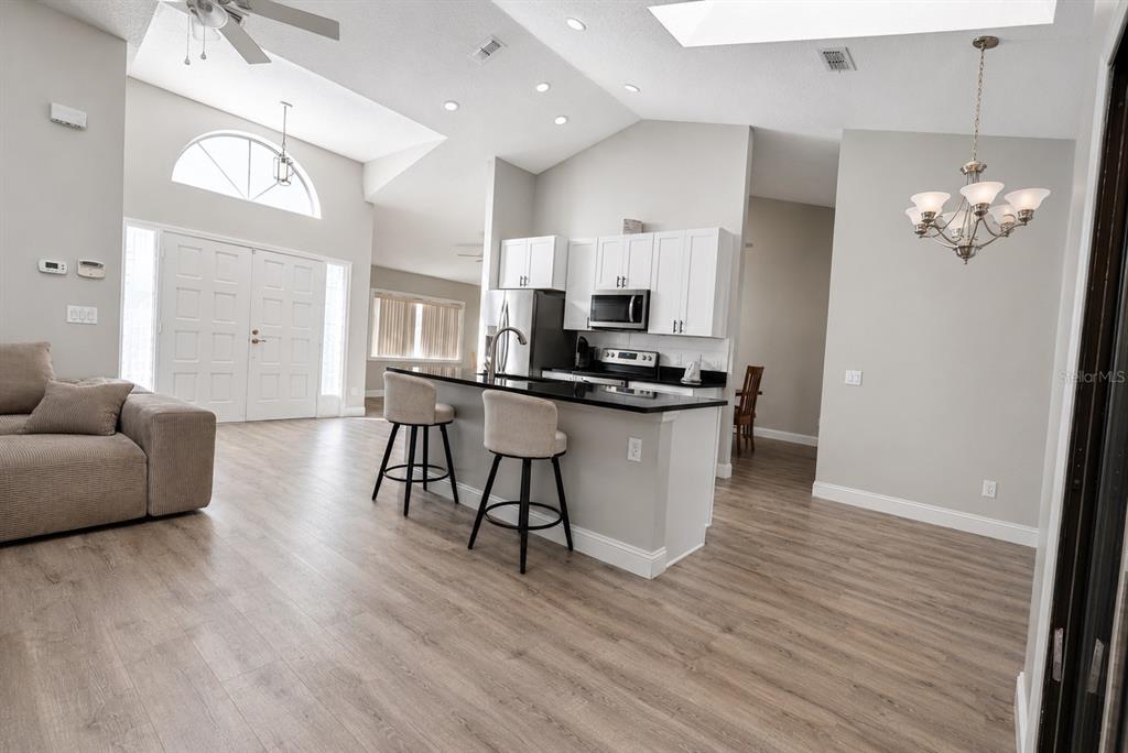 An open-concept kitchen with white cabinets and a black island overlooks a living area — 10 FALLS PLACE, PALM COAST, FL