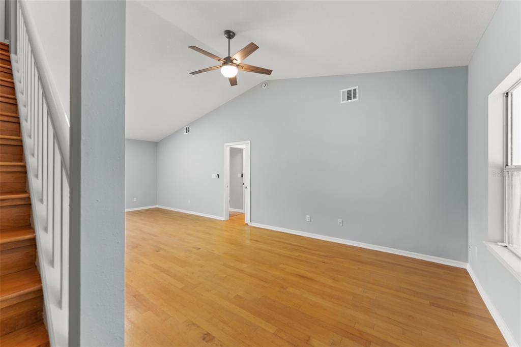 An empty room with hardwood floors, a vaulted ceiling, a ceiling fan, and a staircase — 805 W SMITH STREET, ORLANDO, FL