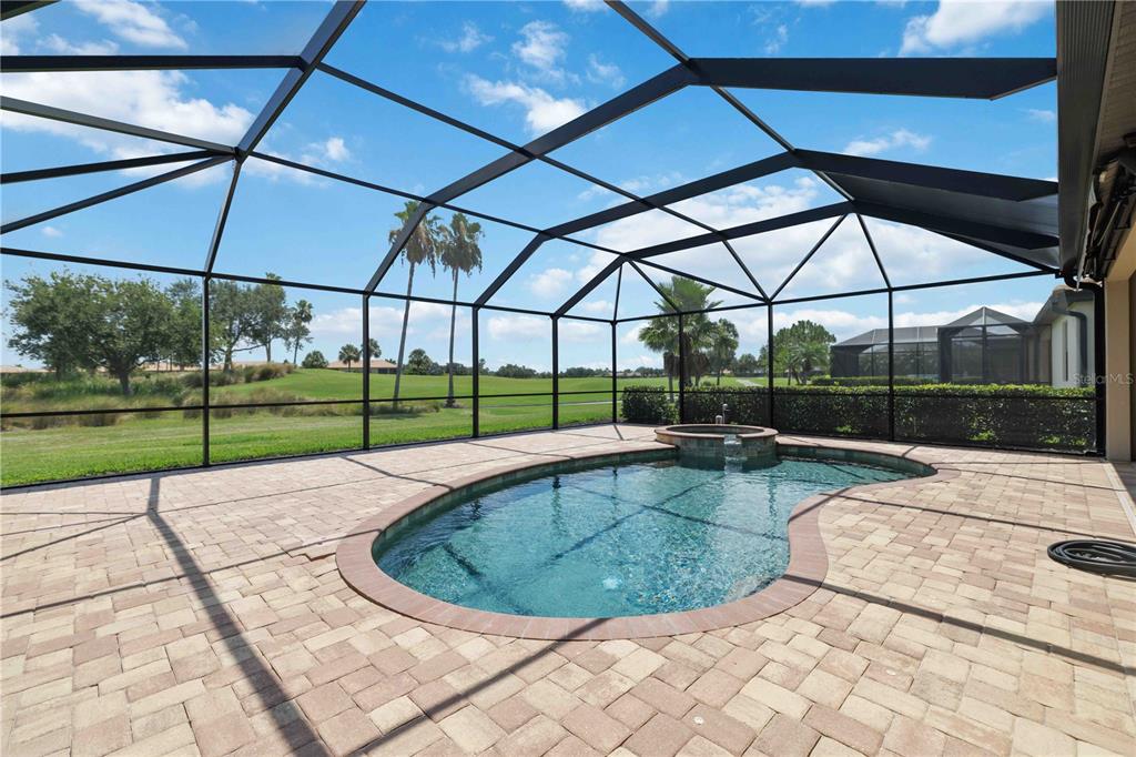 A screened-in patio features a kidney-shaped pool, a hot tub, and paver flooring — 6907 QUIET CREEK DRIVE, BRADENTON, FL