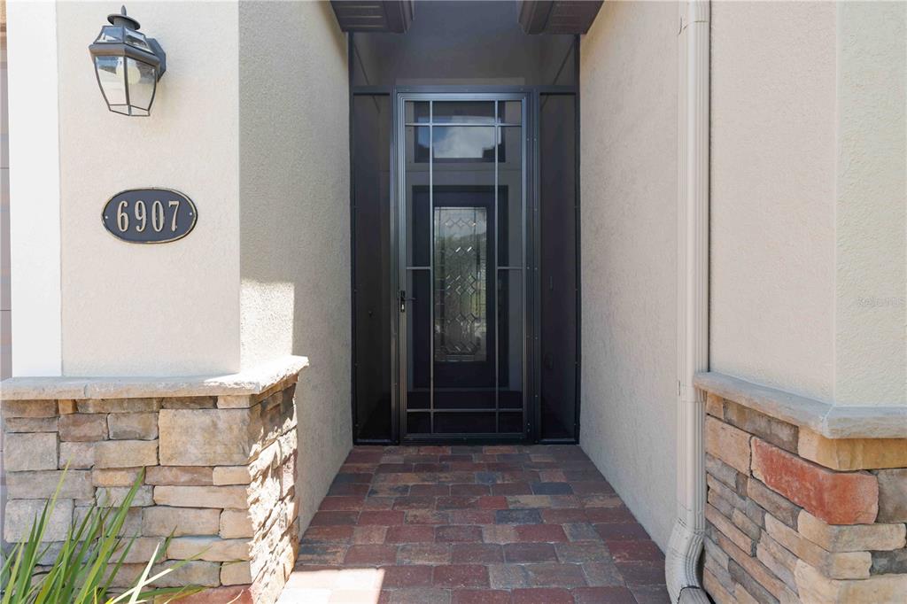 The exterior entryway features a stone-accented wall, a paved walkway, and a dark metal door — 6907 QUIET CREEK DRIVE, BRADENTON, FL