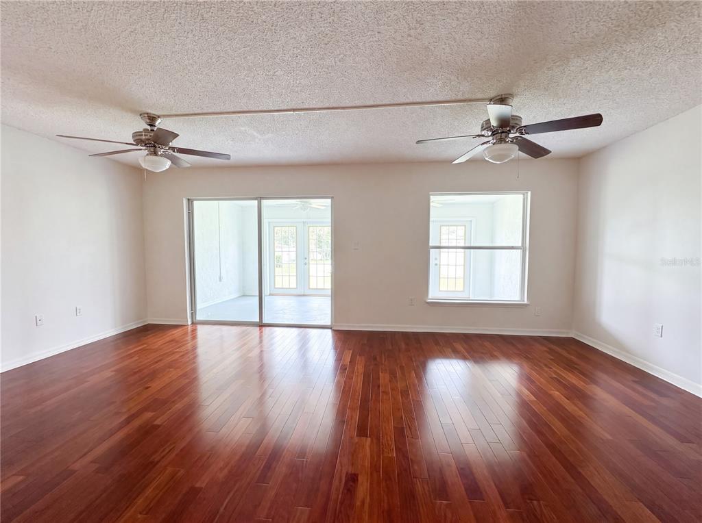 A spacious room features hardwood floors, two ceiling fans, a sliding glass door, and windows — 3538 DAIRY ROAD UNIT 0, TITUSVILLE, FL