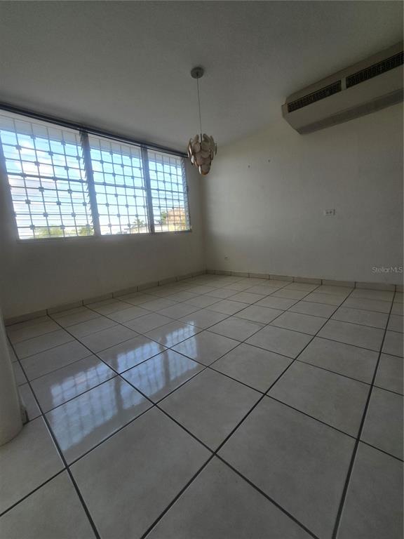 An empty room features white tiled floors, a hanging light fixture, and barred windows — 1608 TAMESIS apt. 201B, SAN JUAN, PR