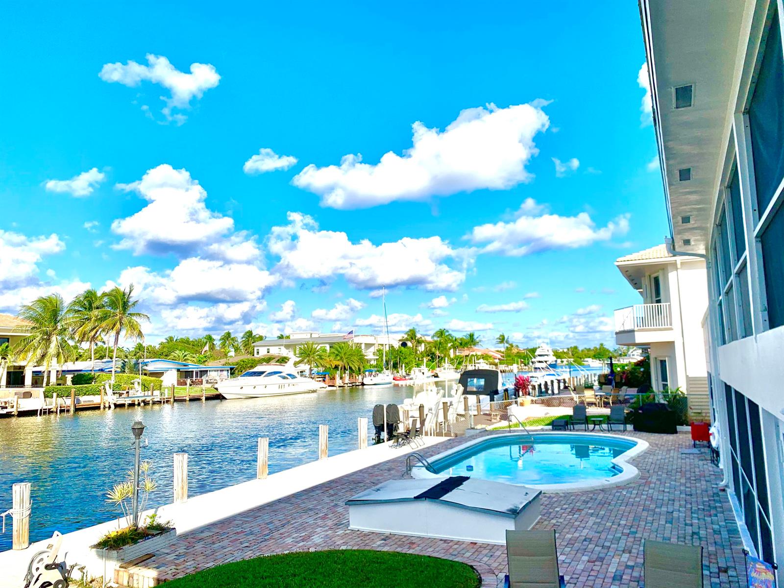 A waterfront patio features a swimming pool, brick pavers, and a view of docked boats — 2735 NE 28 Court, Lighthouse Point FL 33064, LIGHTHOUSE POINT, FL