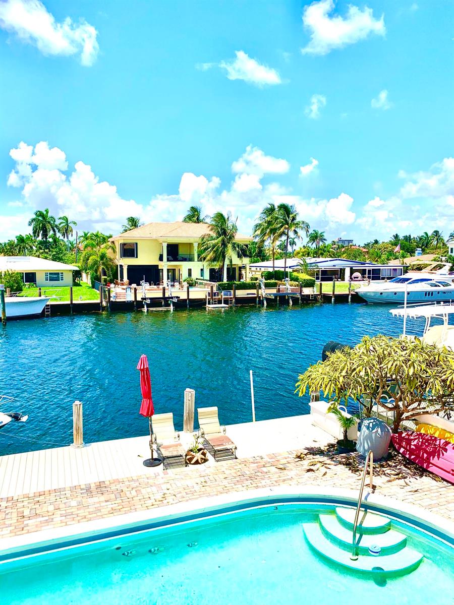 A swimming pool overlooks a canal with a dock, boats, and a two-story yellow house — 2735 NE 28 Court, Lighthouse Point FL 33064, LIGHTHOUSE POINT, FL