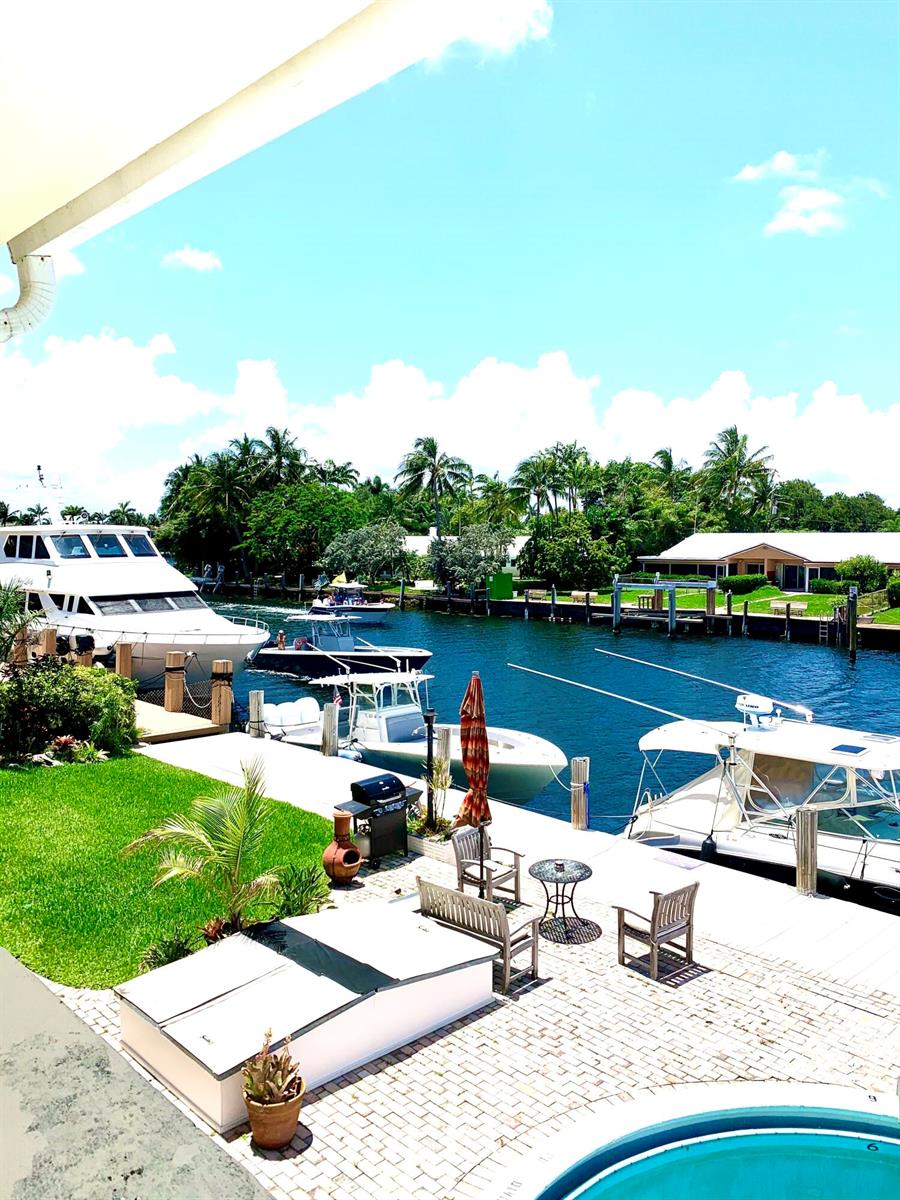 A patio with outdoor furniture overlooks a canal filled with several docked boats — 2735 NE 28 Court, Lighthouse Point FL 33064, LIGHTHOUSE POINT, FL