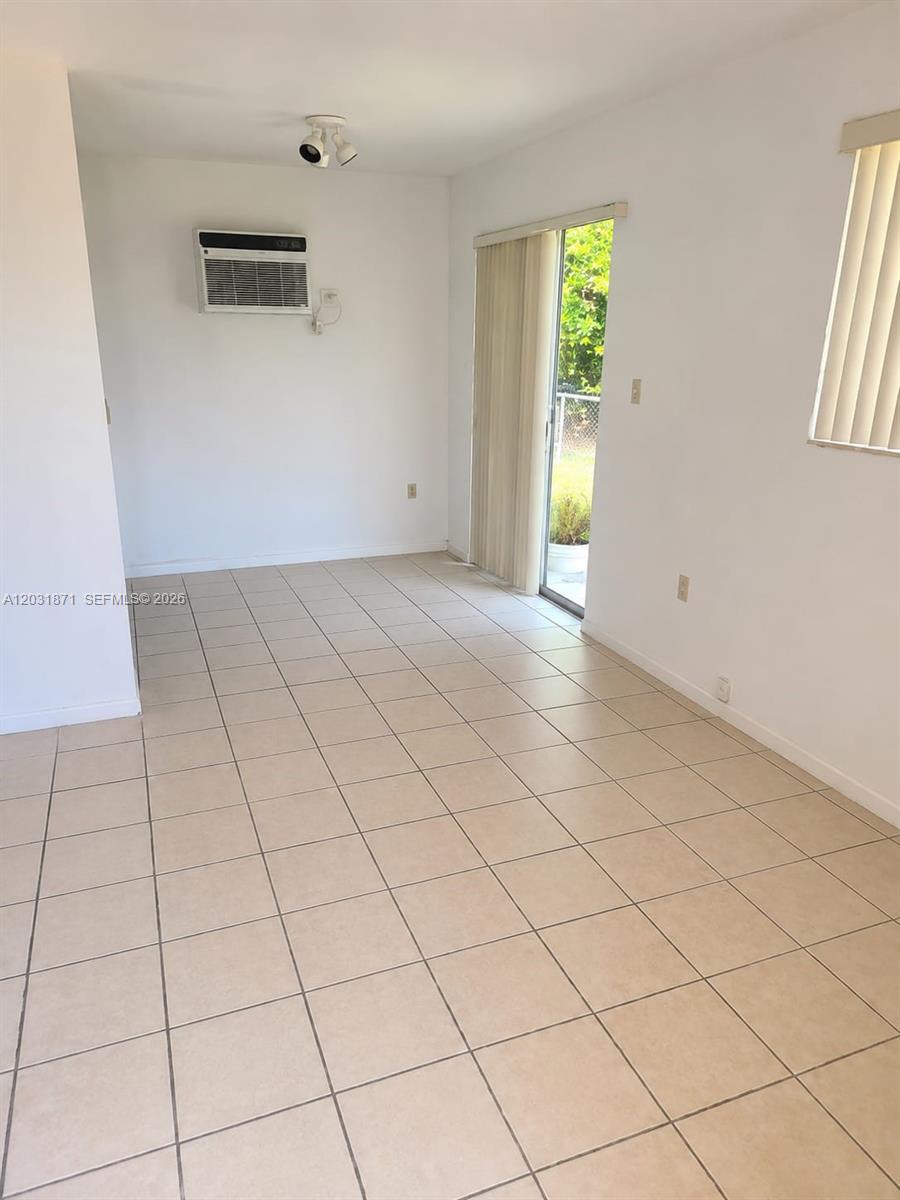 An empty room features beige tile flooring, white walls, a window air conditioner, and sliding doors — 8935 SW 28th St # 8935, Miami FL 33165, MIAMI, FL