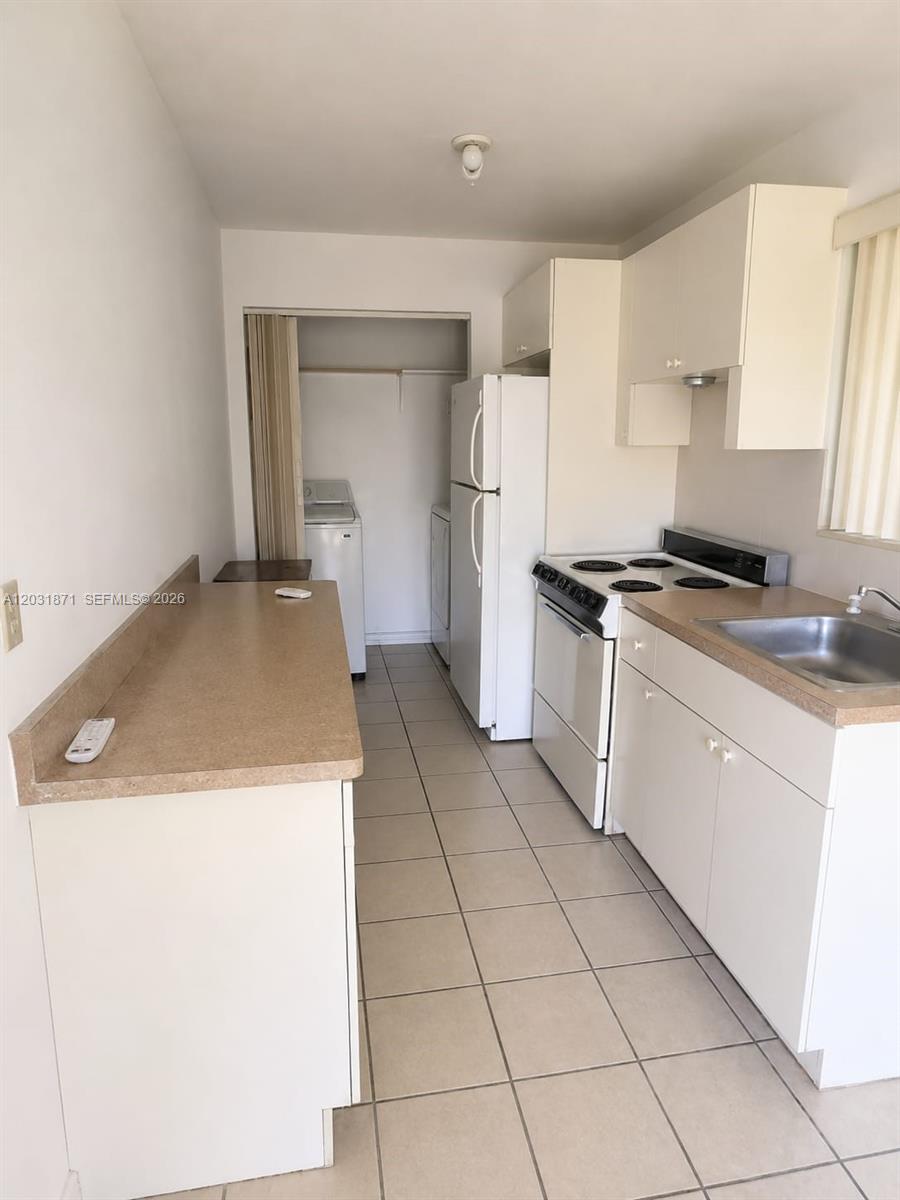 This kitchen features white cabinets, beige countertops, a white appliance suite, and tiled flooring — 8935 SW 28th St # 8935, Miami FL 33165, MIAMI, FL