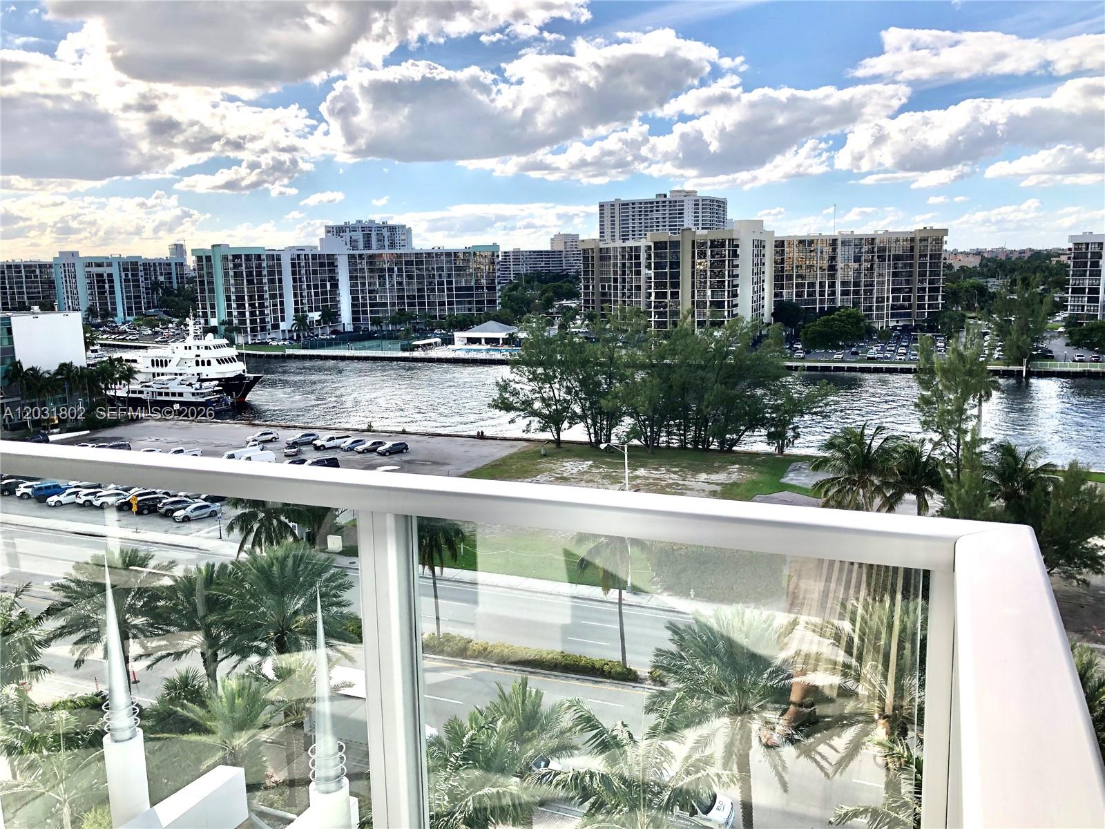 A balcony view overlooks a waterway, parking lot, palm trees, and several large apartment buildings — 3101 S Ocean Dr # 801, Hollywood FL 33019, HOLLYWOOD, FL