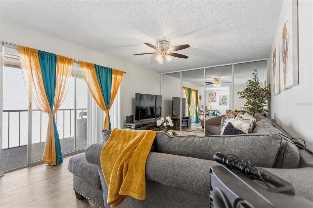 A living room features a grey sectional sofa, mirrored closet doors, and yellow and blue curtains — 7506 PRESLEY PLACE UNIT 113, TAMPA, FL