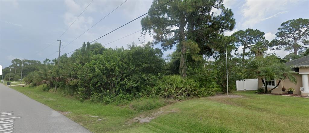 A vacant, tree-covered lot sits next to a residential house with a white fence — FERNWAY DRIVE, NORTH PORT, FL