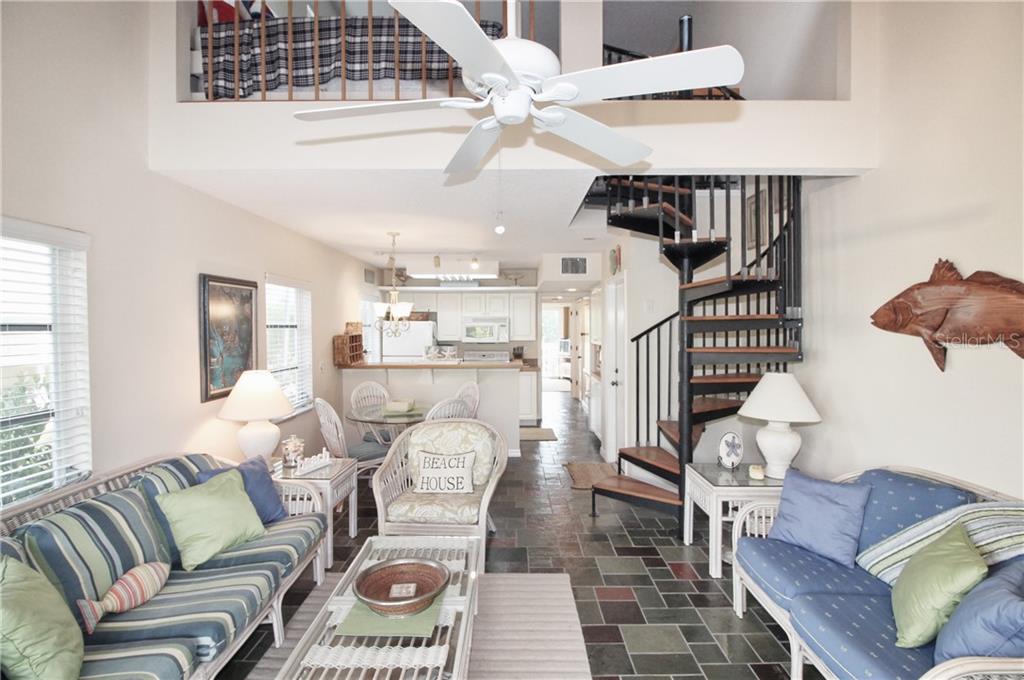 A living room with a spiral staircase, tile flooring, and a loft overlooking the space — 9400 LITTLE GASPARILLA ISLAND UNIT A10, PLACIDA, FL