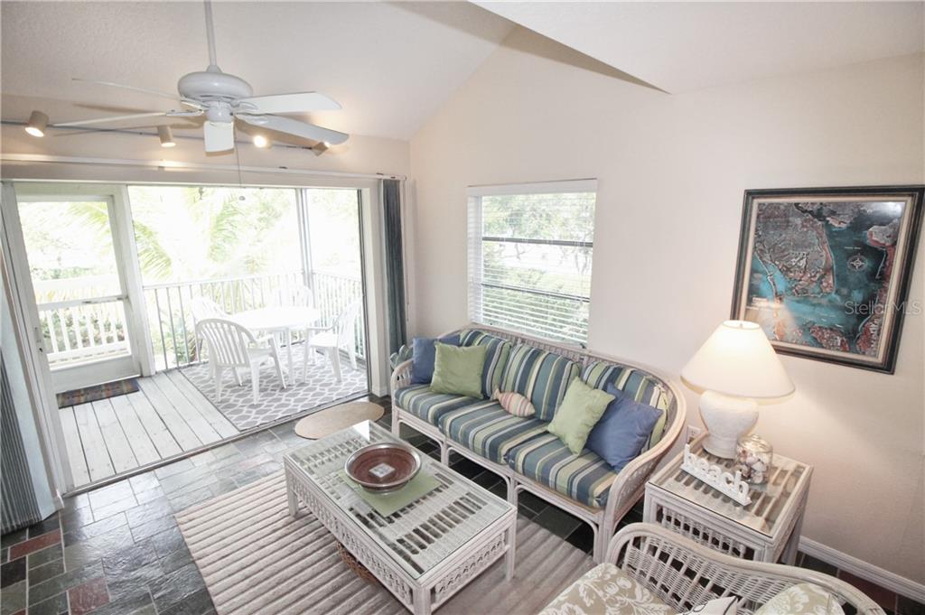 A living room features a striped sofa, glass coffee table, and sliding doors to a balcony — 9400 LITTLE GASPARILLA ISLAND UNIT A10, PLACIDA, FL