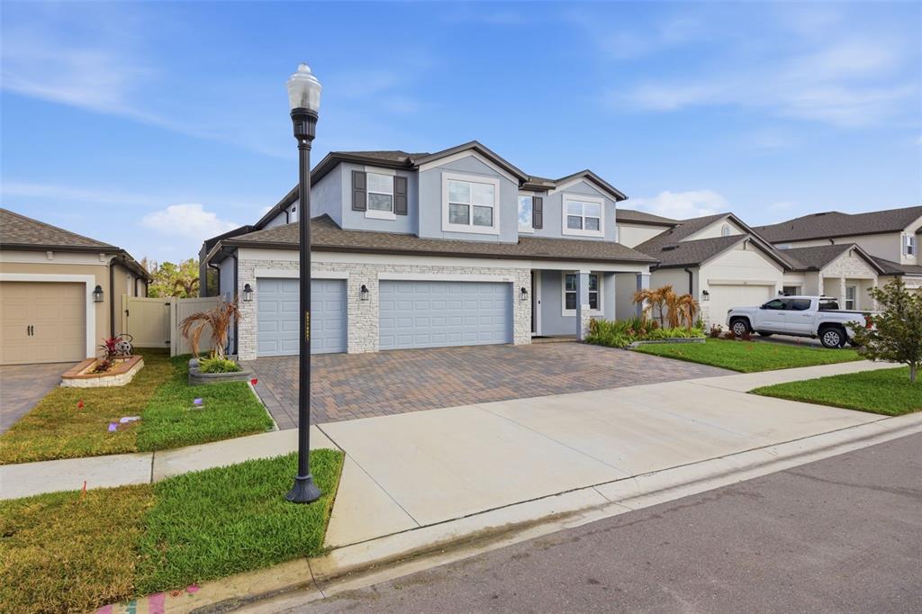 A two-story house with a blue exterior, stone accents, and a three-car garage — 7771 NOTCHED PINE BEND, WESLEY CHAPEL, FL