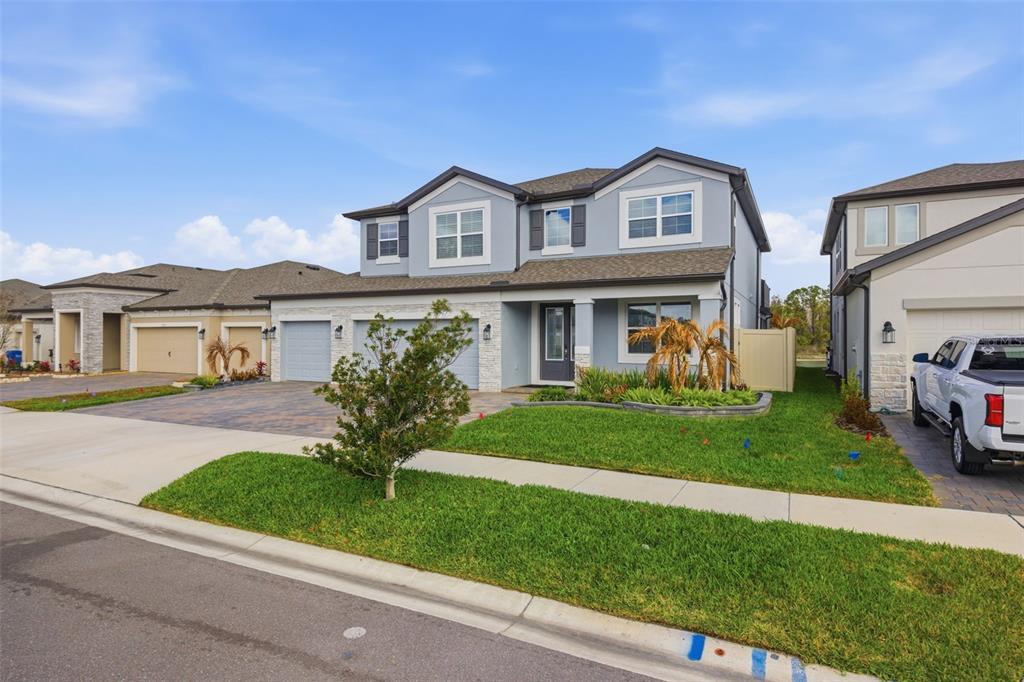 A two-story suburban house with a gray exterior, stone accents, and a paved driveway — 7771 NOTCHED PINE BEND, WESLEY CHAPEL, FL