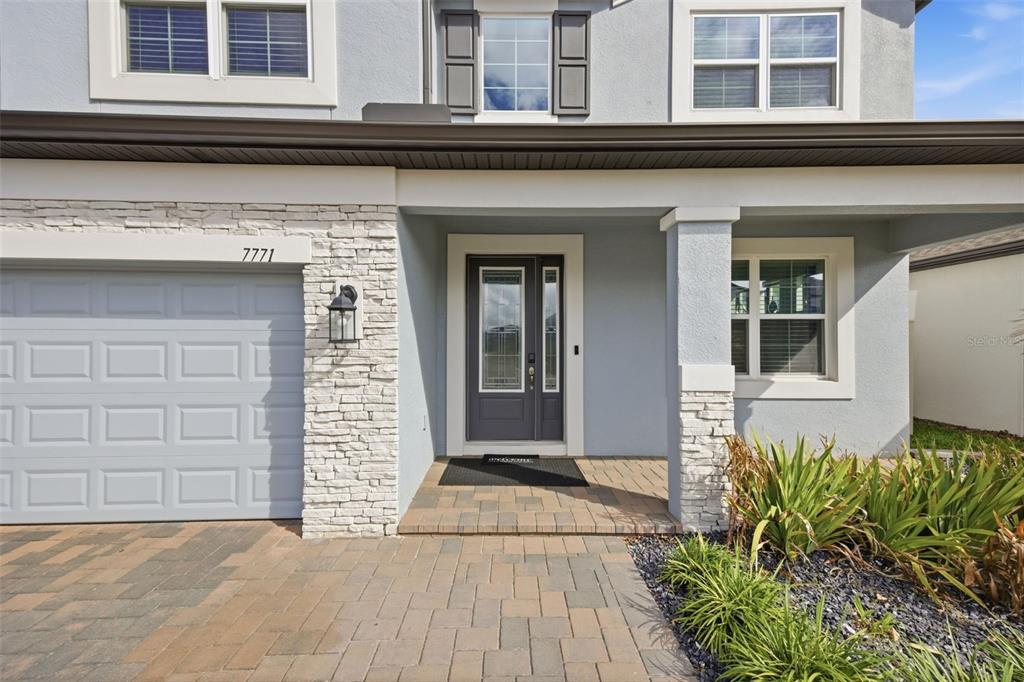 A light blue house exterior features a stone-accented garage, a covered entryway, and a paved driveway — 7771 NOTCHED PINE BEND, WESLEY CHAPEL, FL